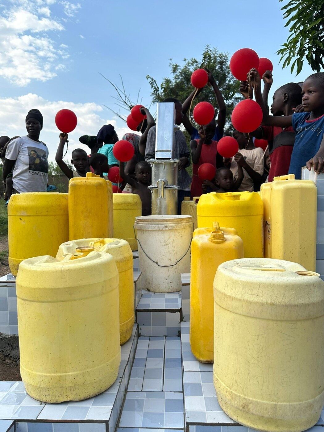 Jerry cans lined up at a newly completed well, decorated with balloons