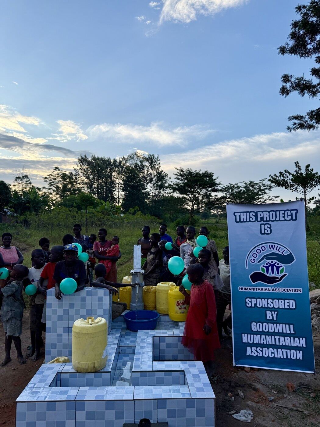 Community members celebrating a newly completed water point at sunset, balloons in hand